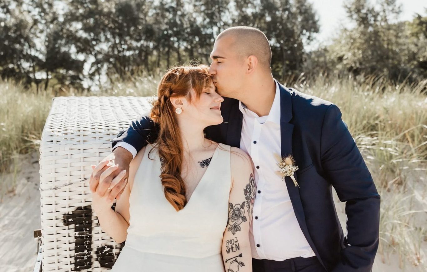 Hochzeit Kühlungsborn Hochzeitspaar am Strandkorb in Kühlungsborn. Der Bräutigam küsst die Braut auf die Stirn.