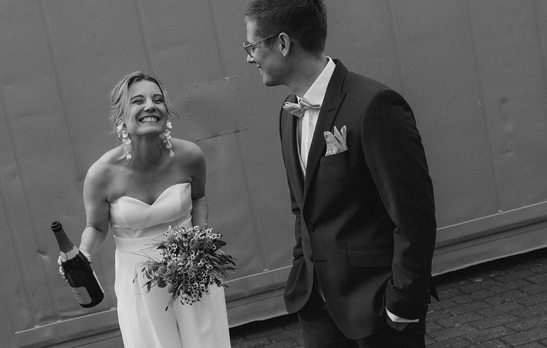 Hochzeitspaar am Stadthafen Rostock Hochzeitspaar am Stadthafen Rostock. Das Paar lacht, die Braut hat eine Flasche Sekt in der Hand und trägt einen Zweiteiler mit Hose & Top.